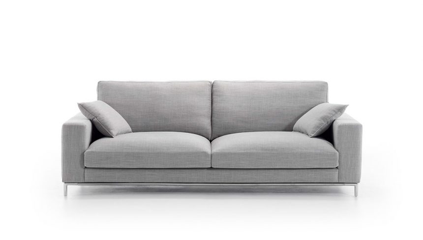 Vista frontal del modelo a fondo perdido de color blanco. Sofá tapizado en microfibra de color gris claro con patas metálicas. Incluye dos cojines de color similar al sofá.
